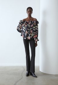 Black off-the-shoulder floral blouse with ruffled neckline, featuring a colorful floral pattern. Paired with fitted dark jeans and pointed ankle boots.