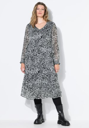 Schwarz-weißer Paisley-Print-Kleid mit langen transparenten Ärmeln, V-Ausschnitt und gestuftem Saum. Kombiniert mit schwarzen knielangen Stiefeln.