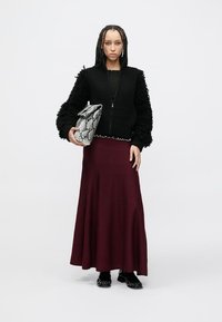 Casaco preto canelado com fecho de correr, mangas texturizadas, saia longa bordô e mala cinza com padrão. Sapatos pretos completam o visual.