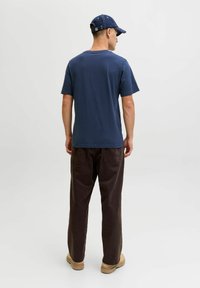 Camiseta de algodón azul marino de manga corta, combinada con pantalones casuales marrones. El conjunto se completa con una gorra oscura. Diseño sencillo, corte relajado.