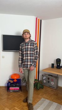 Karirana košulja dugih rukava u smešnoj, crnoj i beloj boji; svetlozelene pantalone; smeđi zamakici; sveukupno ležerna odjeća.