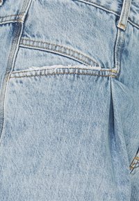 Jasnoniebieskie dżinsy z denimu z fakturowanym wykończeniem, widocznym przeszyciem, kieszenią naszywaną i luźnym krojem.