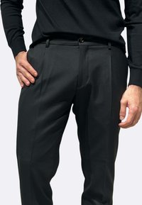 Pantaloni neri su misura con una texture liscia, caratterizzati da un fronte piatto, tasche laterali e una chiusura a bottone singolo in vita.