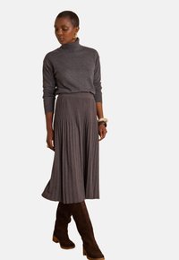 Dolcevita grigio in maglia abbinato a una gonna lunga a pieghe e costine. Stivali marroni in suede al ginocchio con tacchi a blocco completano l'outfit.