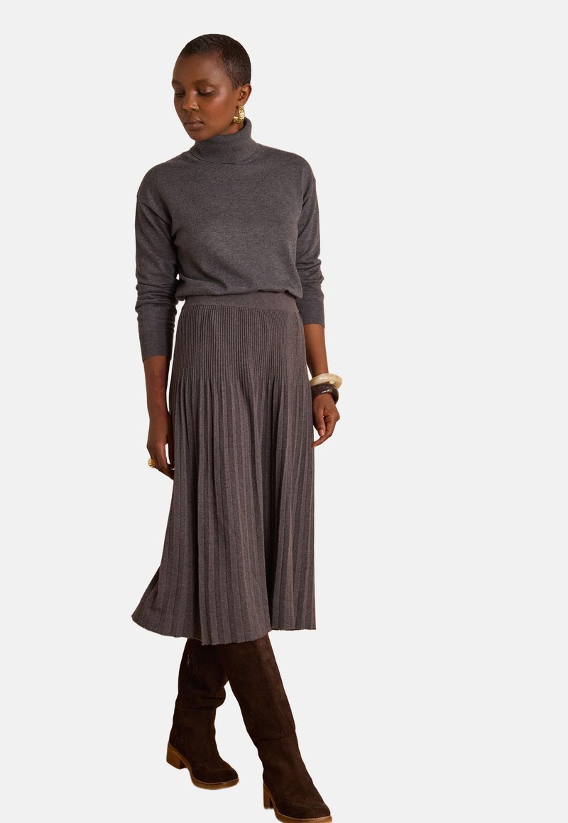 Dolcevita grigio in maglia abbinato a una gonna lunga a pieghe e costine. Stivali marroni in suede al ginocchio con tacchi a blocco completano l'outfit.