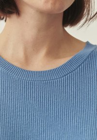 Pull en tricot côtelé bleu avec un large col et un tissu texturé. Vue rapprochée mettant en évidence le matériau et les détails de couture.