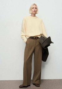 Suéter crema, pantalones de tiro alto marrones de corte holgado, cinturón marrón y una blazer de pata de gallo colgada del brazo. Diseño simple, texturas suaves.