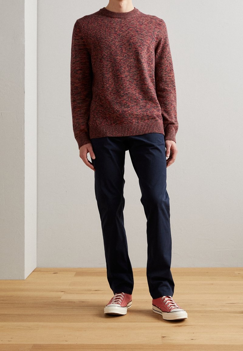 Maglione testurizzato rosso e nero, con scollatura a crew; abbinato a pantaloni blu navy e sneakers rosse con suole e lacci bianchi.