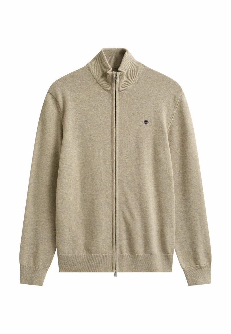 Suéter beige de cremallera completa con cuello, puños y dobladillo acanalados, con un pequeño logo bordado en forma de escudo en el pecho izquierdo.