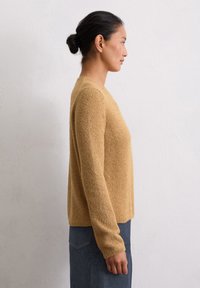 Musztardowy żółty sweter dzianinowy z długimi rękawami i zaokrąglonym dekoltem, o fakturowanej tkaninie, w połączeniu z ciemnoniebieskimi dżinsami.