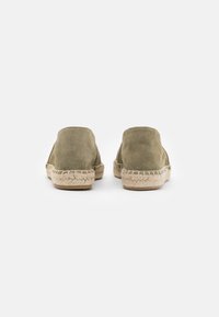 Espadrilles en daim vert avec un dos arrondi, des détails en corde de jute autour de la semelle et une texture lisse et mate.