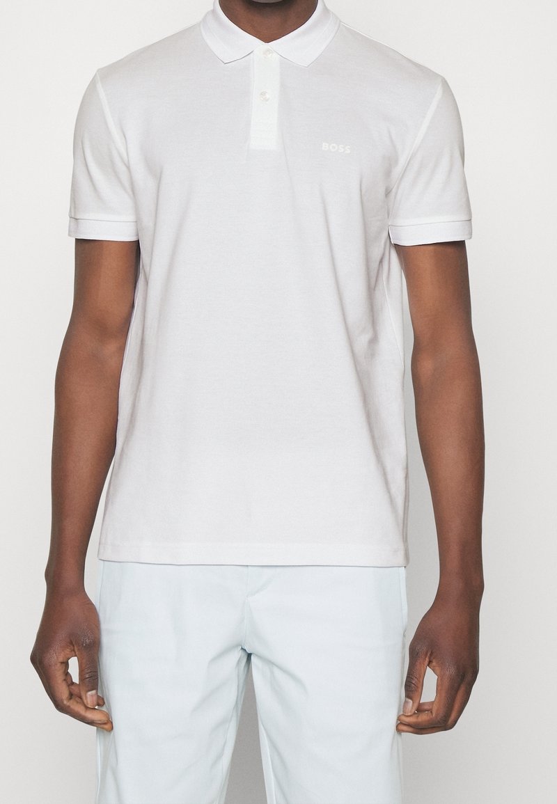 Polo blanc à manches courtes, col, et un logo "BOSS" subtile. Texture douce et coupe standard avec des accents de col contrastants.