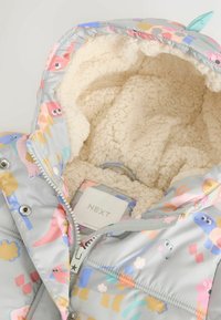Gray padded jacket with colorful animal patterns, plush cream lining, zipper front, and an internal label. Soft texture and playful design.