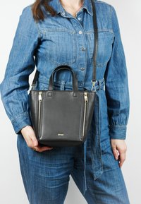 Zwarte leren handtas met bovenhandvatten en een afneembare schouderriem; heeft zilveren ritsen en een gestructureerd oppervlak.