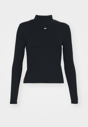 Svart langermet genser med ståkrage laget av glat stoff, med en liten logo i midten av brystet og en tettsittende design.