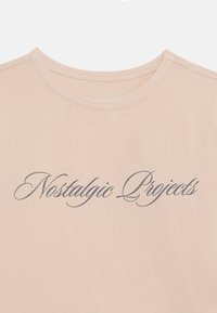 Beżowy t-shirt z okrągłym dekoltem, na piersi napis „Nostalgic Projects” ciemnym kursywą.