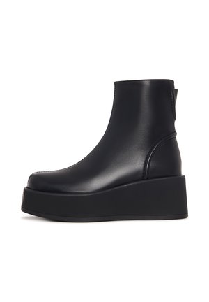 Zwarte enkelboot van soepel leer met een ronde neus en een dikke platformzool, met minimale stiksels en een trekhaak aan de achterkant.