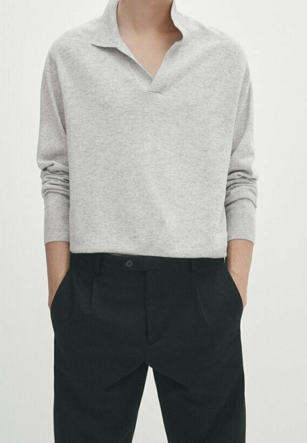Grijze, langwerpige polo met lange mouwen en een V-hals, gecombineerd met zwarte, op maat gemaakte broek. Eenvoudig ontwerp, zachte textuur.
