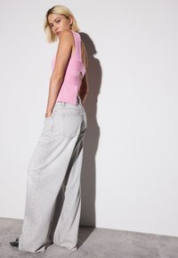 Top rosa sin mangas con diseño de cortes y capas, combinado con jeans de pierna ancha en gris claro. Textura suave, estilo minimalista.