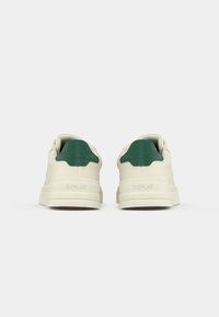 White sneakers with green heel tab. Made of smooth material, featuring a textured sole and brand logo on the back. Low-top design.