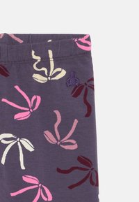 Paarse stof met abstracte strikpatronen in roze, wit en bordeauxrood, en een kleine geborduurde paarse figuur nabij de bovennaad.