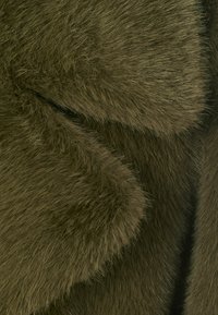 Tessuto in pelliccia sintetica verde oliva con una superficie morbida e testurizzata, caratterizzato da lunghezze di pelo variabili e cuciture lisce. Nessun ulteriore dettaglio visibile.