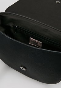Borsa a tracolla in pelle nera testurizzata aperta per mostrare la tasca interna con zip e l'etichetta del marchio Anna Field con chiusura a pressione.