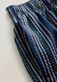 Blue fabric with vertical white, brown, and green stitched stripes, featuring small yellow cross patterns and a gathered waistband detail.