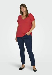 Červený top s krátkým rukávem a kulatým výstřihem, v kombinaci s tmavě modrými skinny džíny a černými plochými botami s dekorativními akcenty.