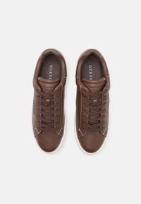 Baskets en cuir marron avec des coutures blanches et des semelles en caoutchouc. Présente un design à lacets et un logo gaufré sur la languette.