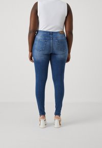 Slim-fit blå denimjeans med bakfickor, midjeresår och en blekt yta. I kombination med vita blockklack-sandaler.