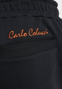 Schwarze Stoff-Jogginghosen mit einem elastischen Bund. Mit einem kleinen, orangefarbenen gestickten Logo "Carla Colucci" im Bereich der Gesäßtasche.