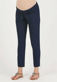 Marineblauwe taps toelopende broek met een elastische tailleband, twee zijzakken en een gladde textuur, gecombineerd met sandalen met kralenaccenten.