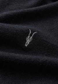 Sort strikket stof med en blød tekstur, prydet med et subtilt gråt broderet kranie-design. Stoffet er glat og let hævet.
