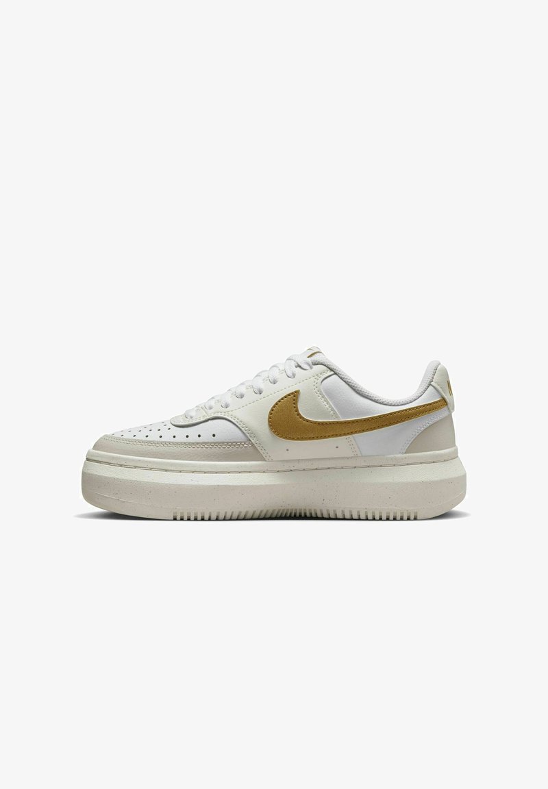 Zapatilla blanca con puntera perforada, swoosh dorado de Nike y suela texturizada. Presenta cordones planos y un cuello acolchado para mayor soporte.