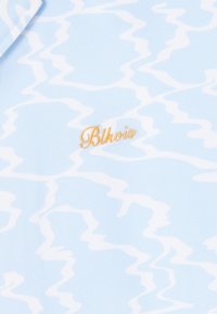 Lichtblauwe stof met een patroon van golvende witte lijnen, met een geborduurd "Blkvis" logo in goud nabij de onderkant rechts. Textuur uiterlijk.