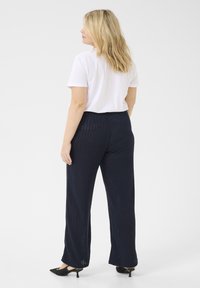 Pantalones de pierna ancha de color navy con textura de costilla vertical, combinados con una camiseta blanca de manga corta. Unos zapatos negros de punta completan el conjunto.