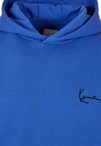 Sudadera azul de algodón, con capucha y cordón ajustable, y un pequeño logo negro en la parte delantera. Textura suave con un diseño casual.