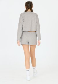 Grijs cropped sweatshirt en bijpassende shorts van zachte stof. De set heeft lange mouwen en een ontspannen pasvorm. Sokken met zichtbare tekst.