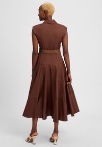 Brown, sleeveless tiered dress with a belted waist. The fabric appears lightweight, featuring a smooth texture and a flowing silhouette.