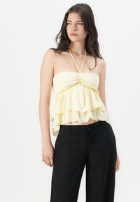 Top strapless galben deschis, cu un design pliat și volane suprapuse la tiv. Puratat cu pantaloni negri, cu croială lejeră.