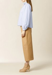 Blusa a righe blu chiaro con maniche voluminose e colletto alla cinese, abbinata a una gonna in pelle alta in vita color marrone chiaro e stivaletti beige.