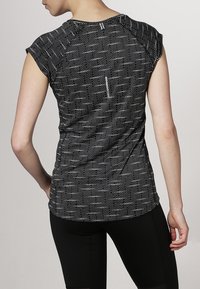 Svart och vit kortärmad topp med ett strukturerat mönster och subtila ränder, och med en dragkedjedetalj i ryggen. Stylad med svarta leggings.