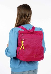 Pink fabric backpack with a textured surface, adjustable straps, and a yellow zipper pull. Contains a front pocket and minimal branding.