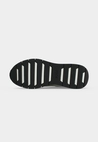 Semelle de chaussure noire avec des rainures rectangulaires blanches et logo "BOSS" embossé au centre, présentée sur un fond gris uni.