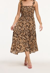 Vestido maxi de patrones marrón, beige y negro con tirantes anchos y detalles de volantes, tela fluida y un corpiño fruncido. Sandalias rosas con tiras.