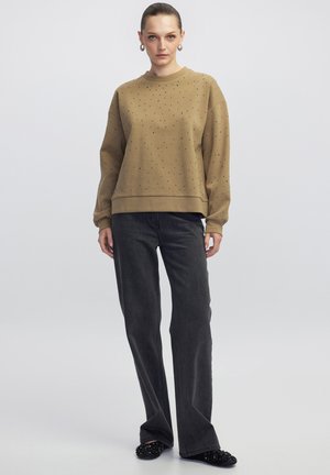 Felpa marrone con decorazioni a pois argentati, scollo rotondo e maniche a polsino, abbinata a jeans a gamba larga grigio scuro e ballerine nere decorate.