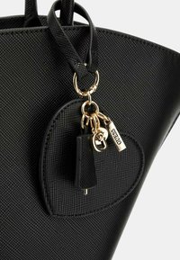 Sac à main noir avec une finition texturée, doté d'un porte-clés en matériel doré, d'un charme rond attaché et d'un petit accent en frange.