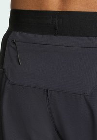 Black athletic shorts featuring a wide waistband and a textured fabric. A rear zip pocket is integrated into the design for secure storage.