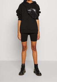 Black oversized hoodie with a graphic, black bike shorts, and black lace-up boots. A small black crossbody bag completes the outfit.